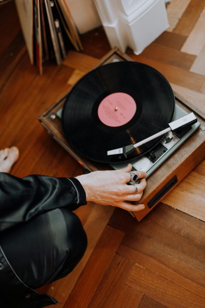 pexels-photo-3693111-3693111 Person adjusting a vintage turntable playing a vinyl record on a wooden floor indoors.